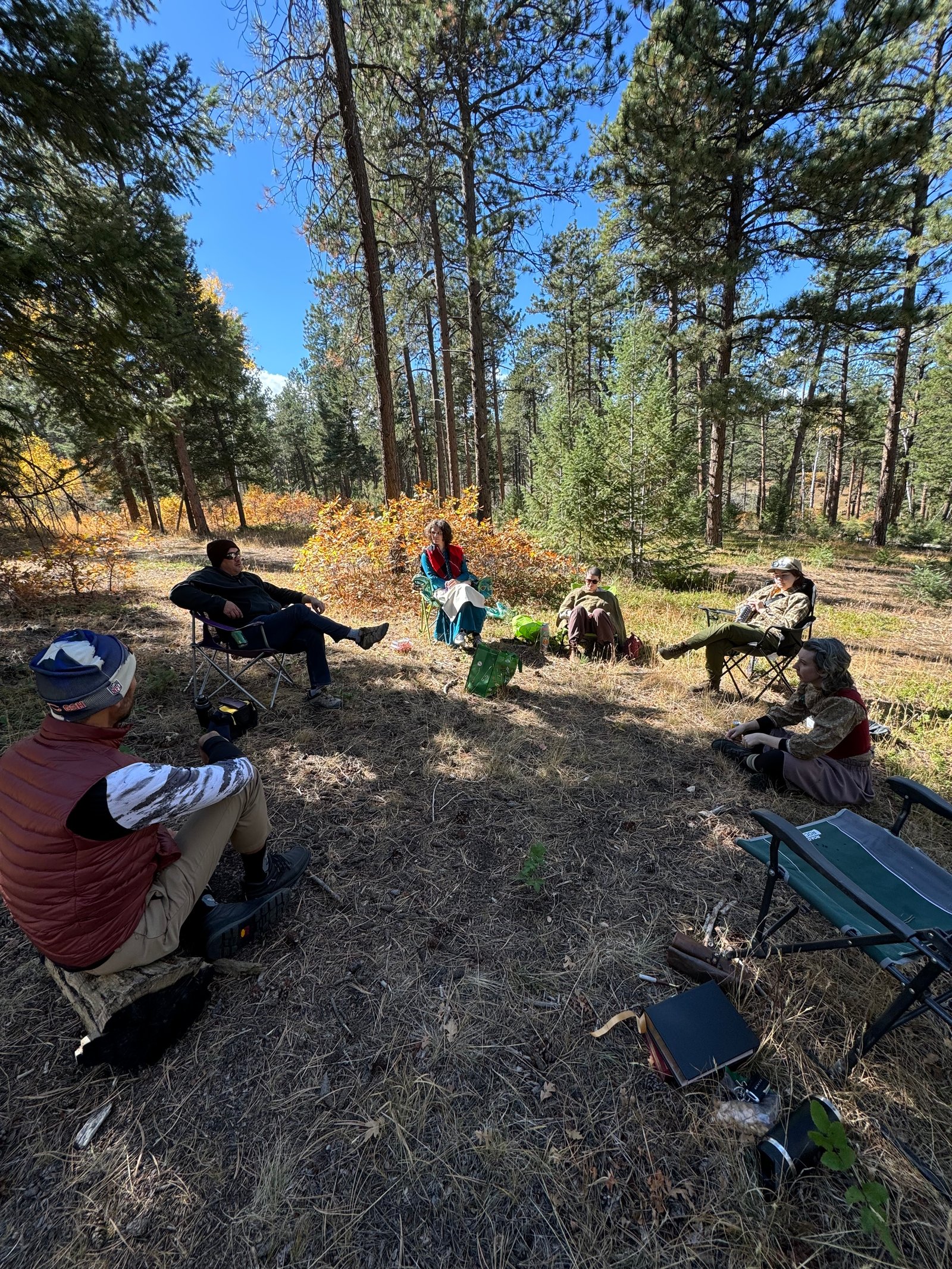 The group gathered in a circle for a woodsie in autumn pines