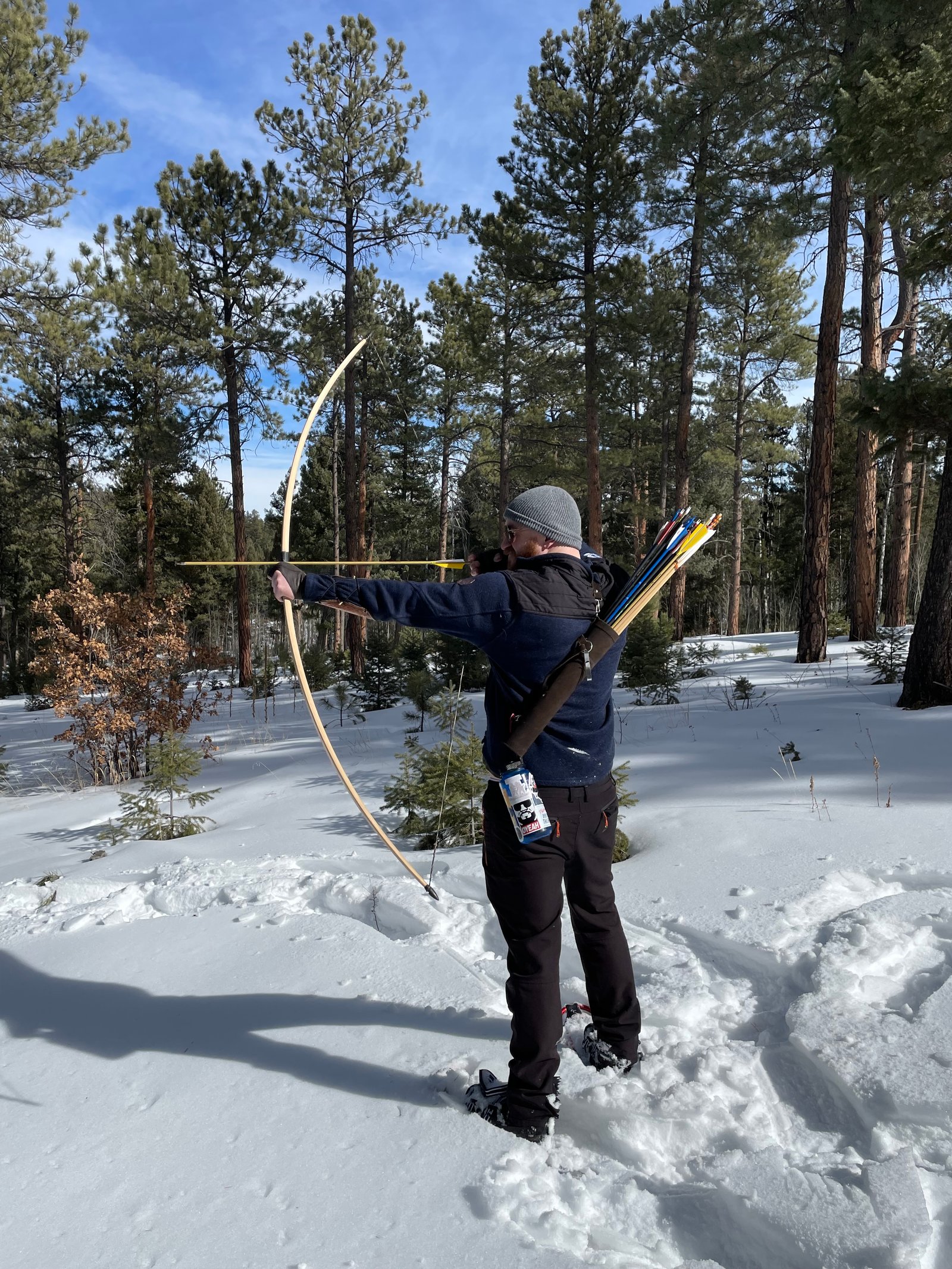 Archer drawing a traditional bow in snowy pines